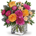 Clear glass cube arrangement of orange roses, hot pink carnations & asters, mini peach carnations, accented with dusty miller &