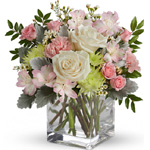 Clear glass cube arrangement of cream/white roses, mid pink spray roses & carnations, soft pink alstroemeria, green cushion spra